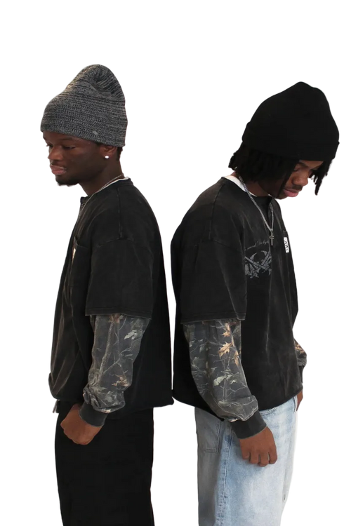 Two people wearing black hoodies and beanies on a plain background