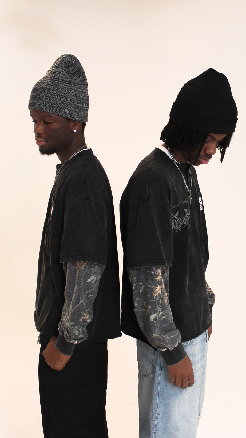 Two people wearing black hoodies and beanies on a plain background